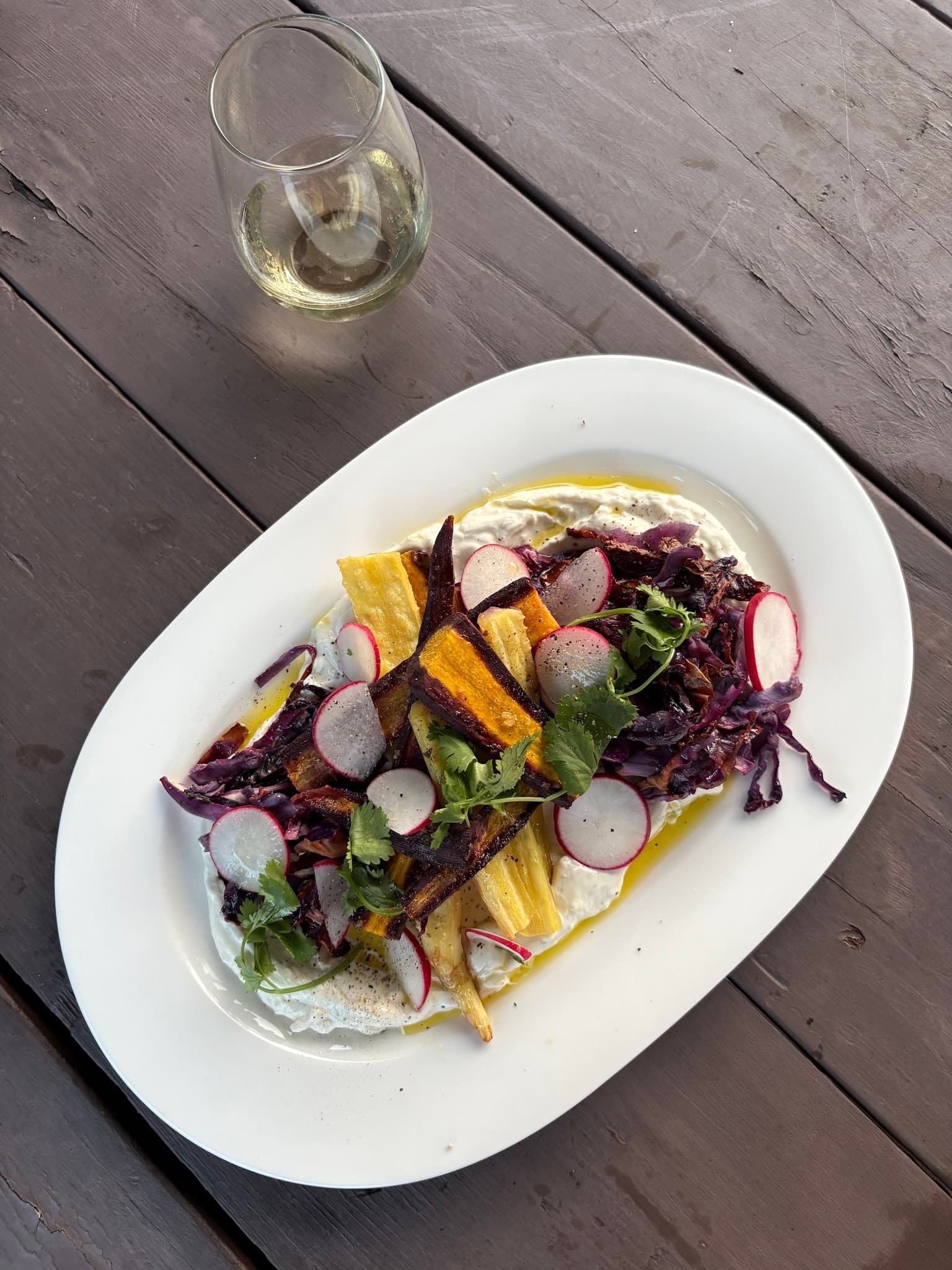 Colorful plated vegetables and greens beside a glass of wine